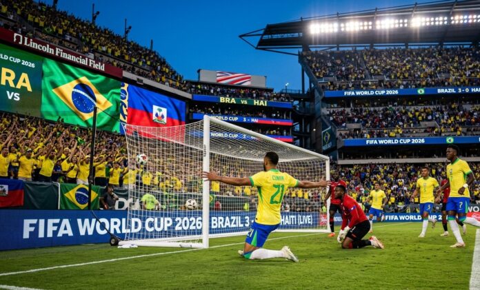 Brazil vs Haiti 2026 World Cup Match Report Brazil forward Matheus Cunha (21) slides on his knees to celebrate a goal against Haiti during the FIFA 2026 World Cup at Lincoln Financial Field in Philadelphia. His arms are spread, smiling towards the fans, while teammates Vinícius Júnior (7) and Neymar Jr. (10) celebrate with him. Large video screens display the 3-0 scoreline.