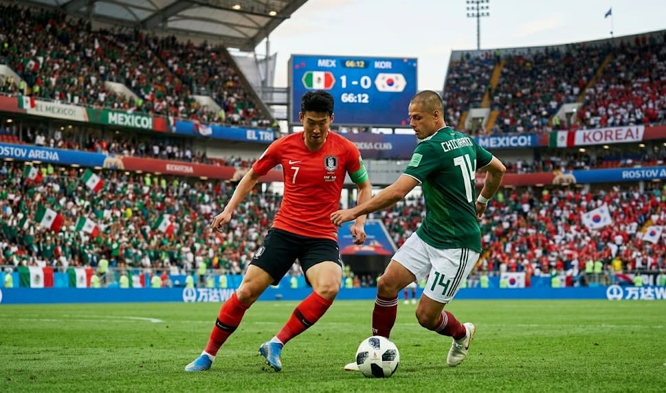 Mexico vs South Korea World Cup Group Stage Clash~2 South Korea's Son Heung-min in a red jersey and Mexico's Javier "Chicharito" Hernández in a green jersey battle for possession of the ball during a World Cup match in a packed stadium.
