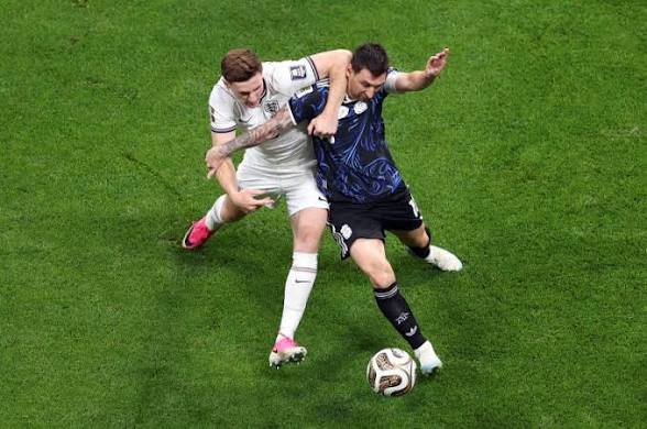 images (75) Lionel Messi, wearing a dark blue Argentina kit, is physically pulled back by England's Elliot Anderson, in a white kit, as they battle for the ball during a soccer match.