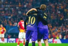 Galatasaray vs Barcelona 1-4: 10 Consecutive Wins Seal Flick’s Flawless Masterclass Two Barcelona players wearing purple away kits with gold lettering, identified as Lamine Yamal and Fermin, hugging on the pitch with a Galatasaray player in the background.